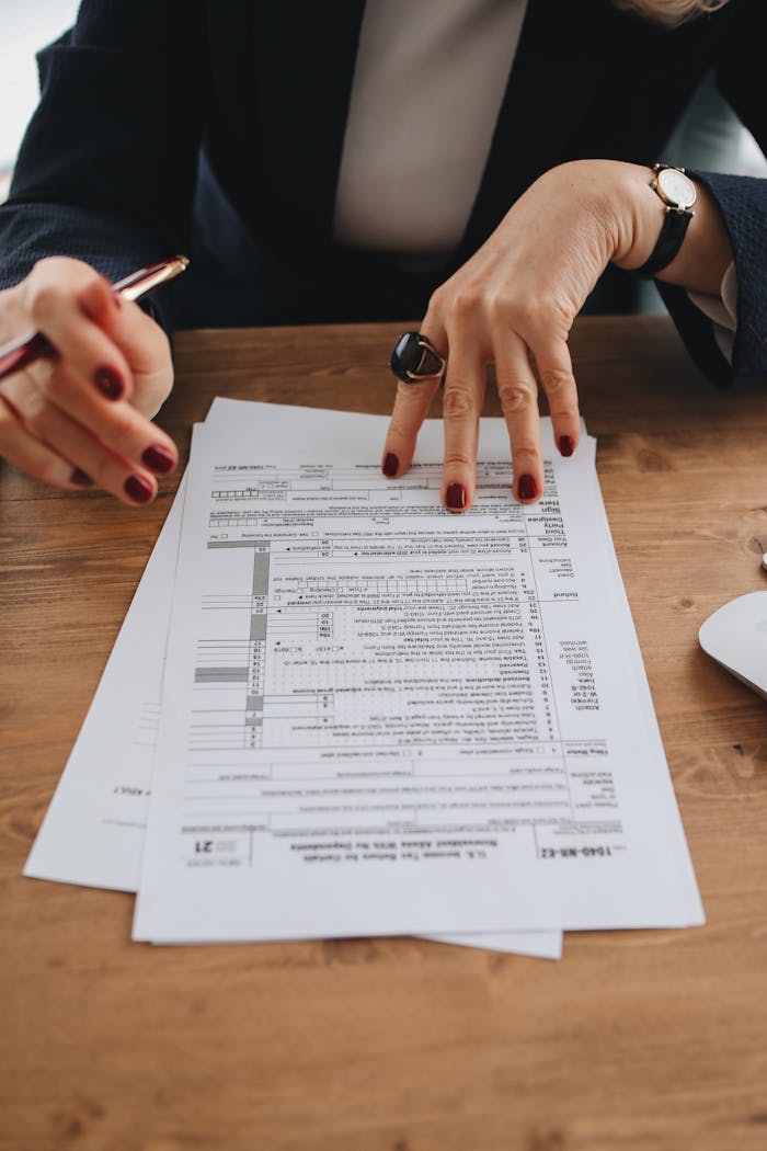 Hands with manicured nails examining tax forms on wooden table indoors.